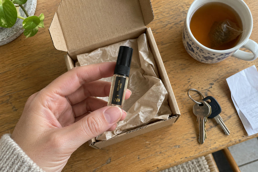 Hand holding an Eesa Solis Noir 3ml perfume sample from an opened postal box on a kitchen table